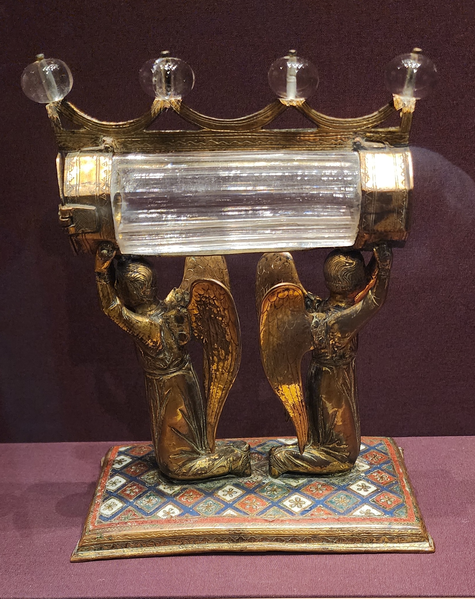 Small reliquary composed of horizontal cylindrical crystal container and a stand that looks like two angels carrying it